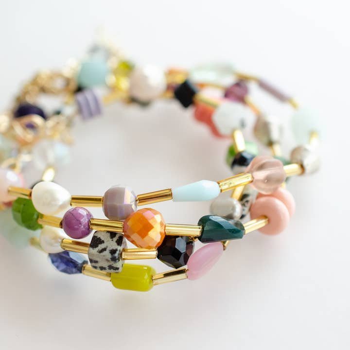 A close-up of the Mariposa Bracelet by Jill Makes shows colorful beaded bracelets with gold tube accents and gemstone beads in varied shapes, sizes, and patterns on a white background.
