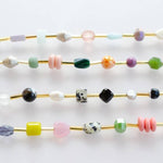 The Mariposa Bracelet by Jill Makes features four gold wires adorned with assorted gemstone beads in round, faceted, and irregular shapes in pastel, bright, and neutral hues, displayed on a white background.