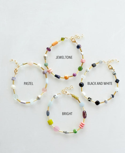 Four Mariposa Bracelets by Jill Makes—pastel, jewel tone, black and white, and bright—are displayed on a white surface, each adorned with colorful gemstone beads for a vibrant accent.