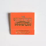 An orange matchbook labeled "Matches | The Incense Match" by The Incense Match with "cinnamon" in gold lettering rests on a white surface—perfect as a compact air freshener and thoughtful incense gift.