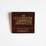 A brown packet labeled "Matches | The Incense Match" by The Incense Match with "coconut" at the bottom sits on a white surface—this innovative air freshener doubles as incense matches, making it an ideal gift for any occasion.