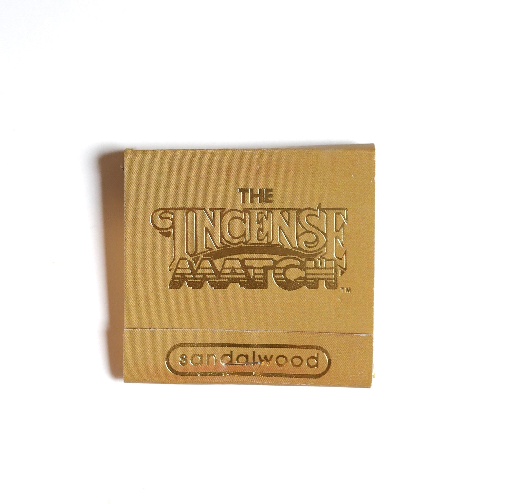 A small brown booklet labeled "Matches | The Incense Match" by The Incense Match, featuring "sandalwood" on the cover, photographed on a white background—ideal as an incense gift or portable air freshener.