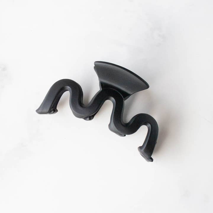 The Matte Waves Hair Clip by Tiepology features a black, wavy matte design with a flat suction base and is displayed on a white surface.