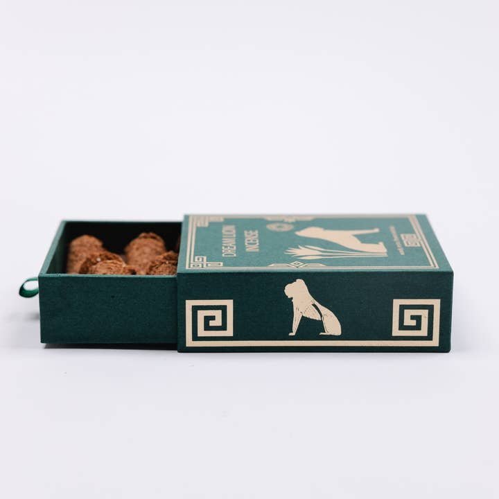 A green rectangular box with gold geometric designs and animal silhouettes, partially open to reveal several Mayan Copal + Desert Sage incense sticks by Dream Lion Incense.