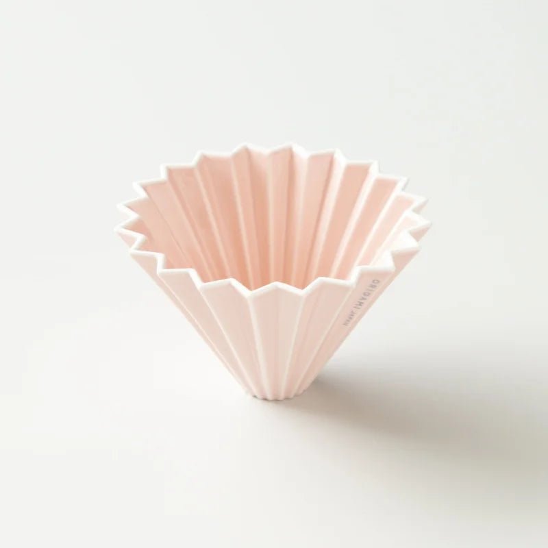 The Medium Dripper by Origami Japan, featuring a pale pink, ridged ceramic pour-over design, sits upright on a plain white surface—perfect for conical filters.