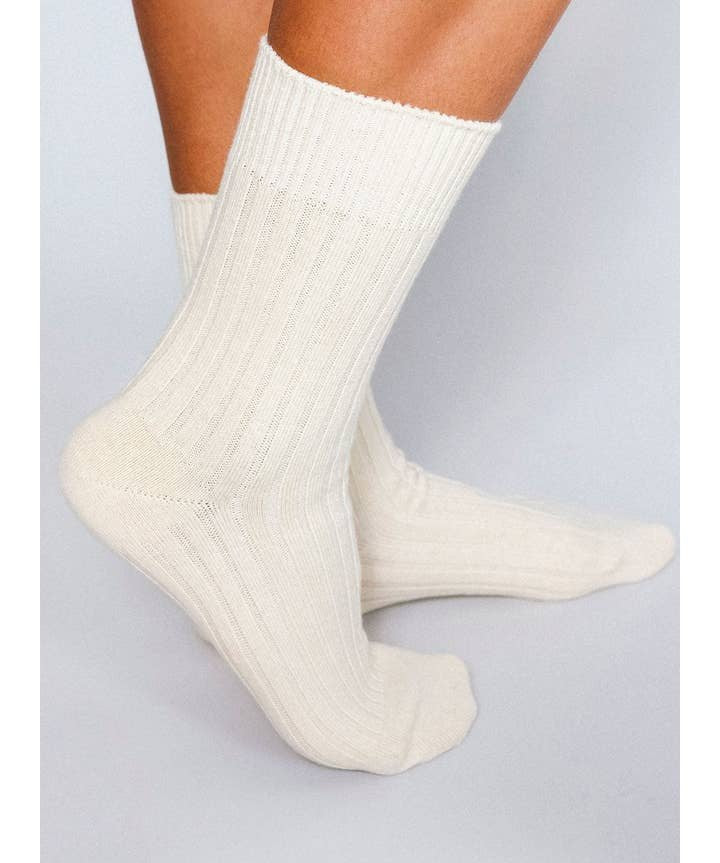 A person wearing Mere Cashmere Ankle Socks by Tailored Union stands on a light-colored surface.