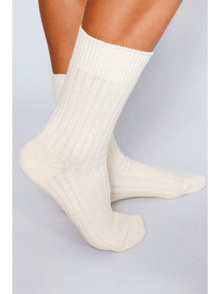 A person wearing Mere Cashmere Ankle Socks by Tailored Union stands on a light-colored surface.