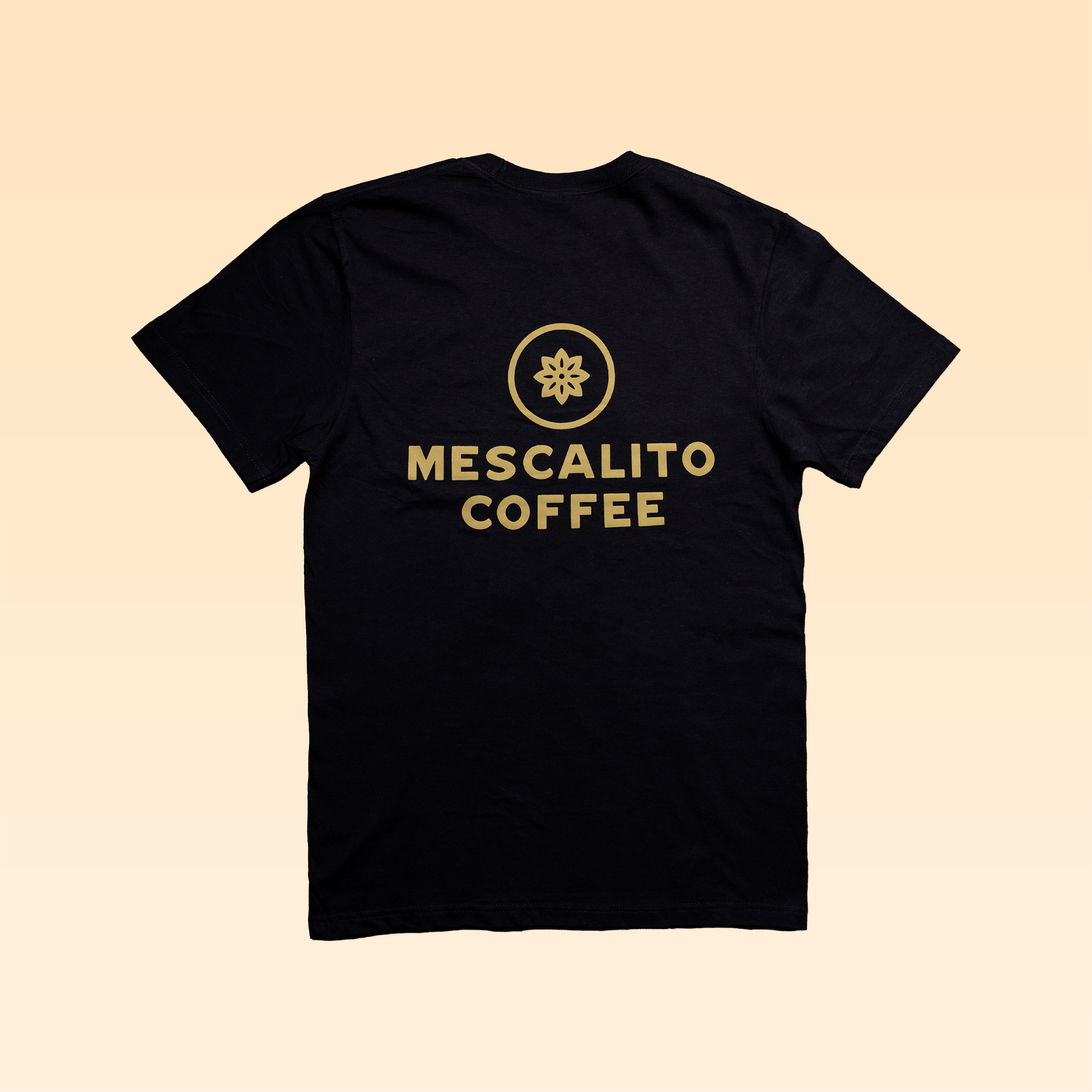 The Mescalito Coffee Shop Shirt by Mescalito Coffee features a gold circular logo and "Mescalito Coffee" on the back, inspired by Brenham’s favorite coffee shop, shown against a beige gradient background.