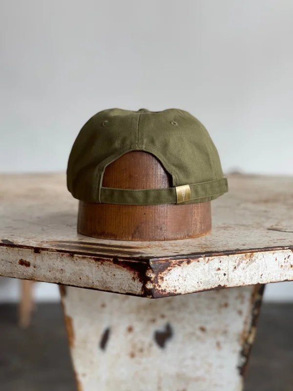 The Mescalito Field Hat by Ballad of the Bird Dog is displayed backwards on a wooden hat stand atop a rustic, worn table.