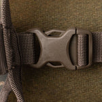 Close-up of a plastic side-release buckle fastened on a woven strap of the Duck Camp Mesh Gear Tote, shown against a brown fabric background.