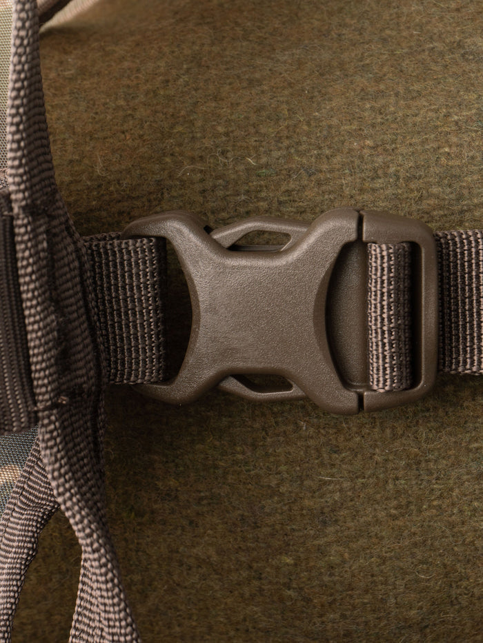 Close-up of a brown plastic side-release buckle fastened to a webbed strap on the Duck Camp Mesh Gear Tote, secured against its textured fabric.