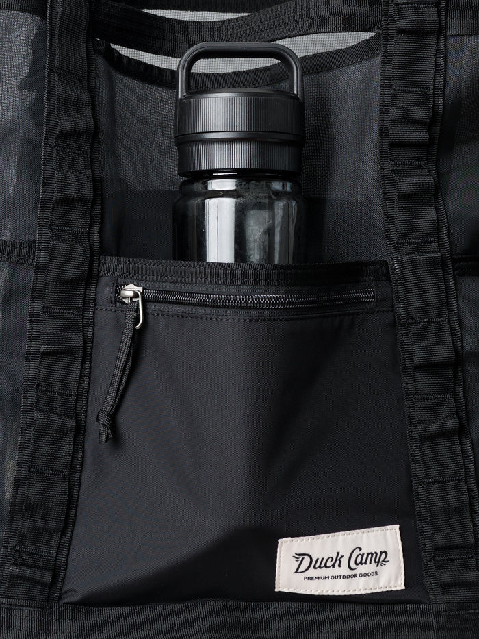 A black water bottle in the Duck Camp Mesh Gear Tote, featuring a front zipper pocket and Duck Camp brand label—a water-resistant mesh bag ideal for outdoor adventures.
