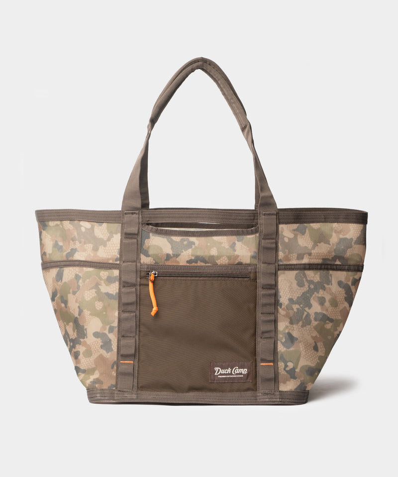 The Mesh Gear Tote by Duck Camp features a camouflage pattern, dual handles, front zip pocket with orange pull, and Duck Camp logo—perfect for carrying your essentials on any adventure.