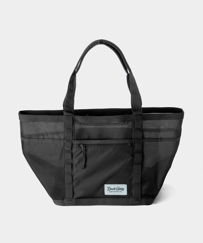 The Duck Camp Mesh Gear Tote is a black mesh bag with two handles, a front zipper pocket, and a Duck Camp patch on the front, shown against a plain light background.