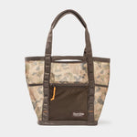 The Mesh Gear Tote by Duck Camp is a water-resistant, camouflage bag with brown handles, trim, front zipper pocket, and Duck Camp logo—ideal for outdoor adventures.