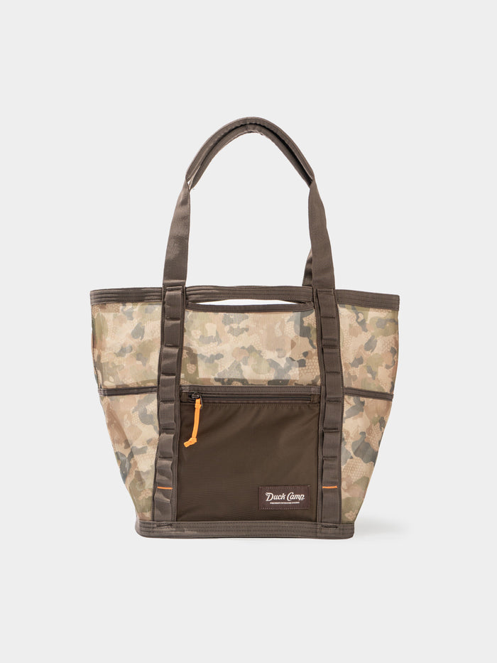 The Mesh Gear Tote by Duck Camp features a camouflage pattern, brown handles, front zip pocket, small Duck Camp logo, and water-resistant design to keep your essentials protected wherever you go.