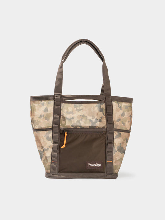 The Mesh Gear Tote by Duck Camp features a camouflage pattern, brown handles, front zip pocket, small Duck Camp logo, and water-resistant design to keep your essentials protected wherever you go.