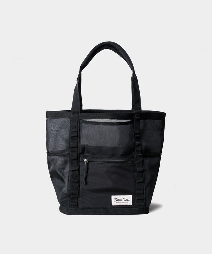 The Mesh Gear Tote by Duck Camp is a durable black mesh bag with two handles, front zippered pocket, side mesh pockets, and a rectangular white patch label—ideal as an outdoor storage tote for all your essentials.