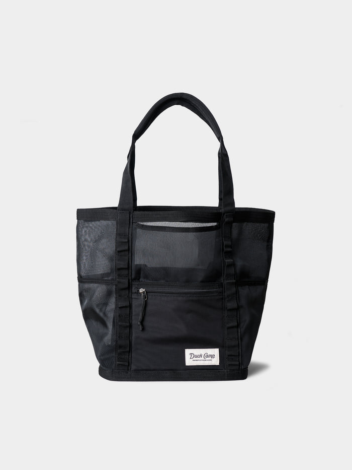 The Mesh Gear Tote by Duck Camp is a durable black mesh bag with two handles, front zippered pocket, side mesh pockets, and a rectangular white patch label—ideal as an outdoor storage tote for all your essentials.
