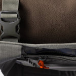 Close-up of a gray strap with a plastic buckle on the Duck Camp Mesh Gear Tote, featuring a textured brown body and a partially open zippered pocket with an orange pull.