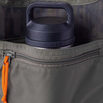 A gray Yeti water bottle is partially visible inside the open pocket of a Duck Camp Mesh Gear Tote, which features a heavy-duty design and an orange zipper pull.