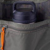 A dark-colored YETI water bottle partially tucked into the zippered pocket of a gray Mesh Gear Tote by Duck Camp, featuring an orange pull tab.