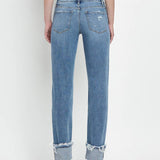 A person wears Vervet’s Mid Rise Cuffed Straight Jean, made from comfort stretch denim with frayed, rolled cuffs and visible back pockets. The jeans show light distressing for a casual vibe and are viewed from the back.