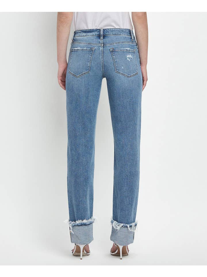 A person wears Vervet’s Mid Rise Cuffed Straight Jean, made from comfort stretch denim with frayed, rolled cuffs and visible back pockets. The jeans show light distressing for a casual vibe and are viewed from the back.