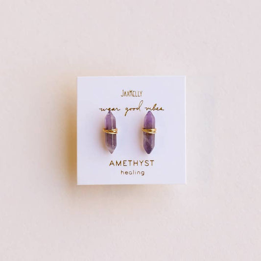 A pair of Mineral Point Amethyst Gold earrings by JaxKelly, featuring double point amethyst crystals wrapped in gold wire, displayed on a white card labeled "JaxKelly" and "Amethyst healing.