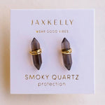 The JaxKelly Mineral Point Smoky Quartz earrings feature double point smoky quartz stones wrapped in gold wire on a branded "Wear Good Vibes" and "Protection" card. Hypoallergenic for comfortable wear.