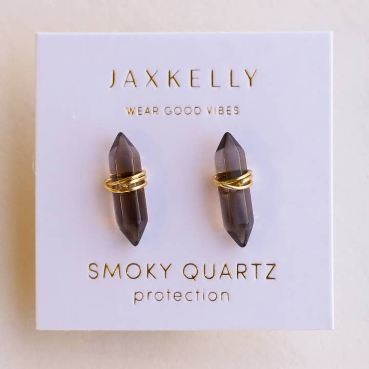 The JaxKelly Mineral Point Smoky Quartz earrings feature double point crystals and gold wire wrapping, presented on a white "Wear Good Vibes" and "Protection" JaxKelly card. Hypoallergenic for elegant style and positive energy.