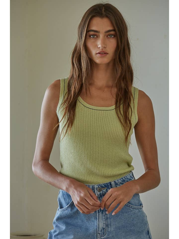 Woman with long brown hair wears the Mira Sleeveless Top by By Together in light green, paired with blue denim jeans, standing against a plain, light-colored background.