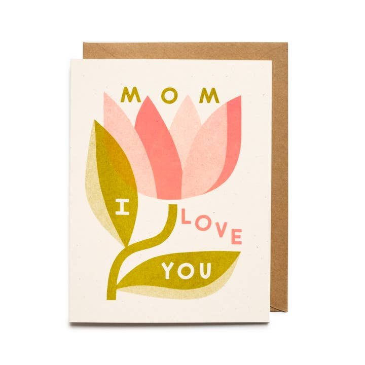 The Mom I Love You Card by Worthwhile Paper features a pink flower with "Mom I Love You" on its petals and leaves, plus an envelope behind the card—a perfect Mother’s Day greeting from the Worthwhile Cards collection.