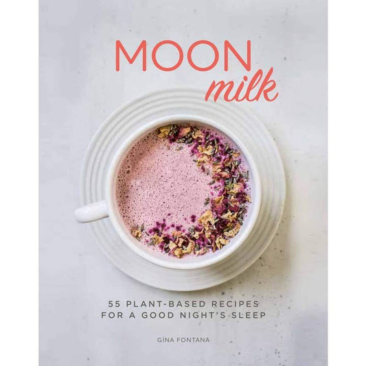 A white cup of pink Moon Milk, a soothing insomnia remedy, is topped with dried flowers on a saucer beside the book "Moon Milk" by Union Square and Co.