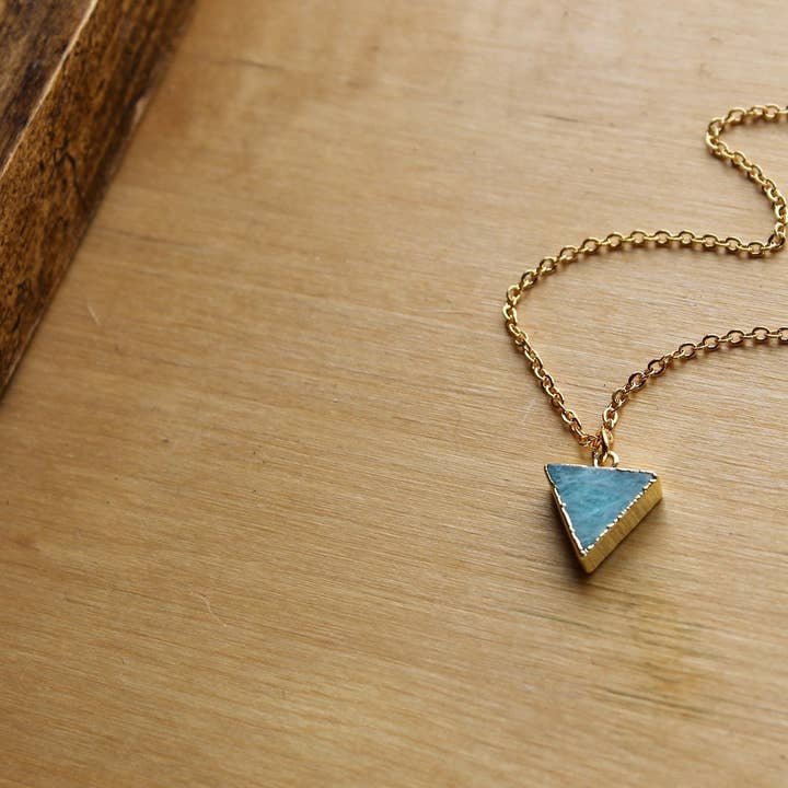 The Vintage Acorn "Amazonite Triangle" necklace features a 16K gold plated chain with an amazonite pendant and gold filled spring clasp, displayed on wood beside a box.