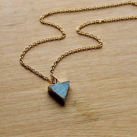 The Vintage Acorn Necklace | Amazonite Triangle features a light blue triangle-shaped amazonite stone pendant on a 16K gold plated chain, secured with a gold filled spring clasp and displayed on wood.