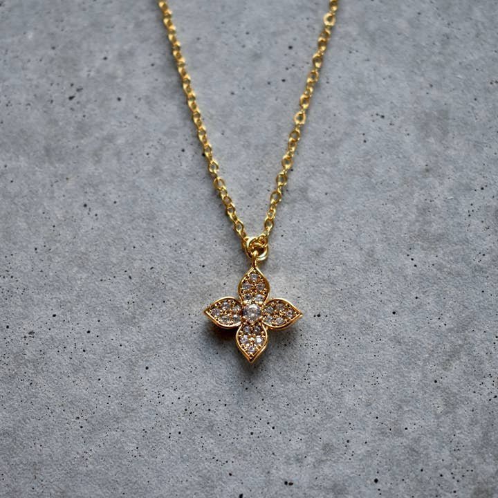 The Vintage Acorn Necklace | Crystal Flower features a gold chain with a flower-shaped cubic zirconia pendant, adorned with clear stones and secured by a gold-filled spring clasp, shown on a gray textured surface.