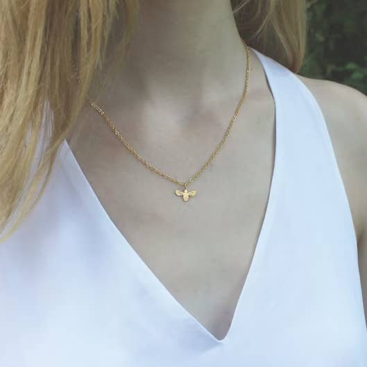 A woman wears a white sleeveless top and the Vintage Acorn Gold Bee Necklace, featuring a small 16K gold plated pendant.