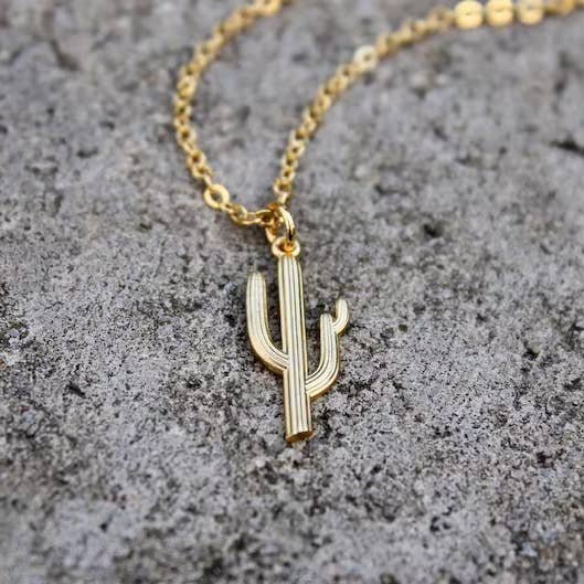 The Vintage Acorn Saguaro Cactus Necklace features a 16K gold-plated, nickel-free cactus pendant, shown on a textured gray stone, perfect for comfortable everyday wear.