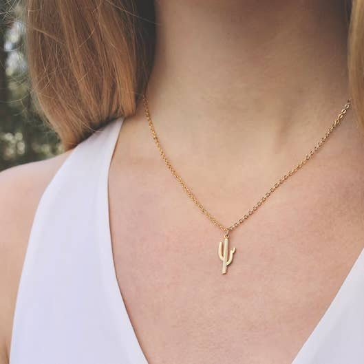 A person wears a white sleeveless top and the Vintage Acorn Necklace | Saguaro Cactus, a 16K gold plated, nickel and lead free piece featuring a cactus pendant.