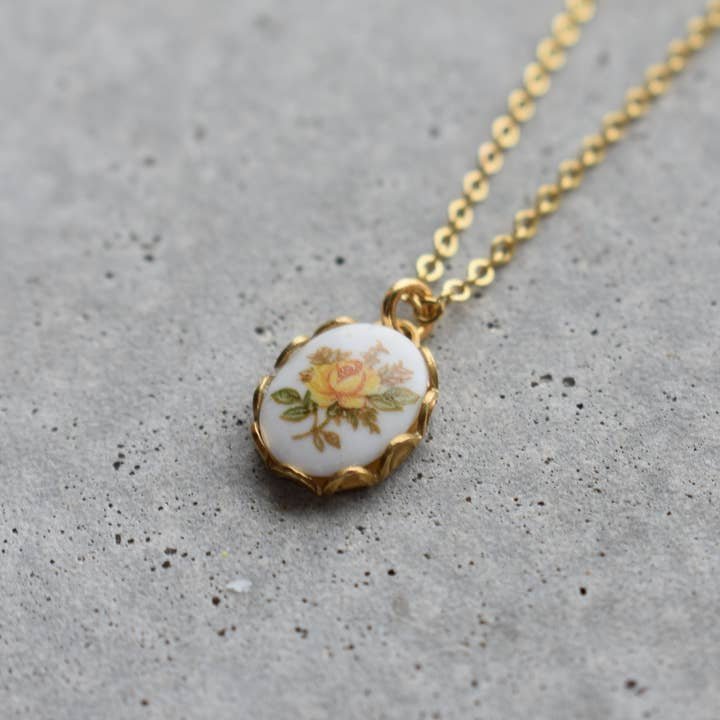 The Necklace | Vintage Floral by Vintage Acorn features a 16K gold plated pendant with a yellow and orange floral design on white, gold filled spring clasp, is nickel and lead free, and shown on a gray textured surface.