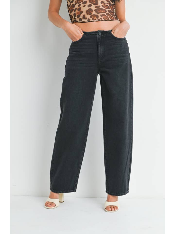 A person wearing JBD's No Waistband Low Rise Straight jeans in washed black, paired with a leopard print crop top and white heeled sandals, stands against a white background.