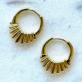 The Nova Earrings by Jessica Matrasko Jewelry are small gold filled spike huggies featuring a row of vertical gold bars on one side, displayed on a light textured surface. Hypoallergenic and perfect for everyday elegance.