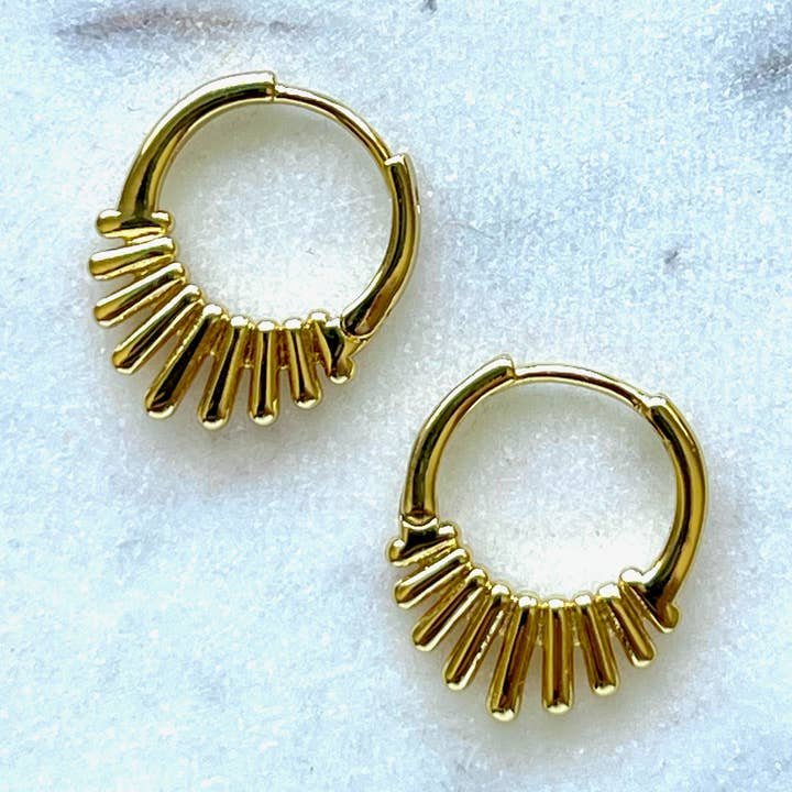 The Nova Earrings by Jessica Matrasko Jewelry are small gold filled spike huggies featuring a row of vertical gold bars on one side, displayed on a light textured surface. Hypoallergenic and perfect for everyday elegance.