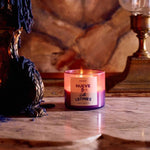 A lit Roen Nueve Leones coconut soy wax candle rests on marble beside a melted blue candle and a brass lamp, highlighting the elegance of hand-poured candles in reusable jars.