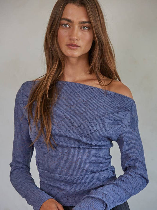 A woman with long brown hair wears the By Together Off The Shoulder Top, featuring textured blue lace, standing against a neutral background.