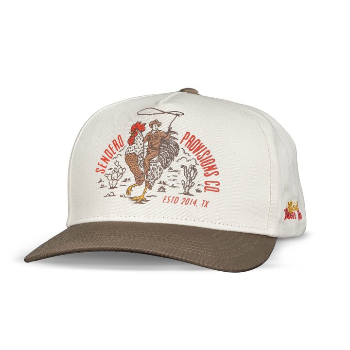 The Official Western Hat by Sendero Provisions Co. is a white and brown embroidered cap with a cowboy riding a rooster, desert plants, and “Sendero Provisions Co. ESTD 2014, TX” on the front.