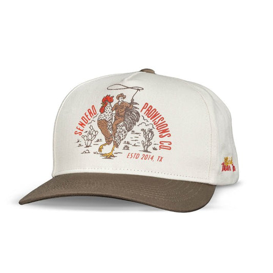 The Official Western Hat by Sendero Provisions Co. is a white and brown embroidered cap with a cowboy riding a rooster, desert plants, and “Sendero Provisions Co. ESTD 2014, TX” on the front.