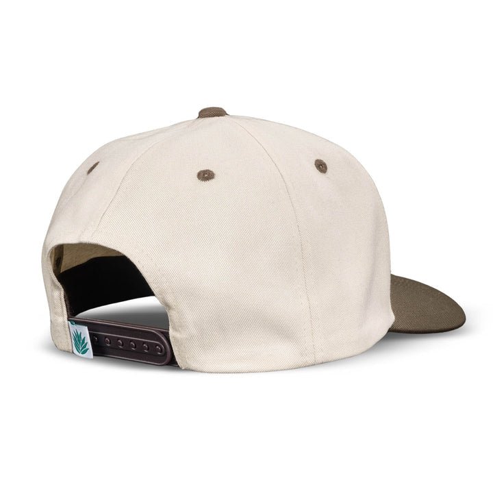 The Official Western Hat by Sendero Provisions Co. is a beige and brown snapback cap shown from the back, featuring an adjustable strap and a small leaf patch near the closure.