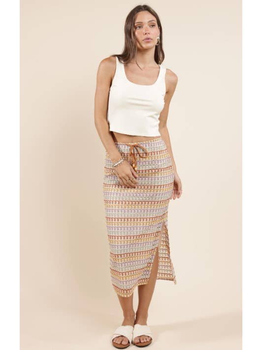 Woman wears the On My Mind Easy Crop Tank by Sadie And Sage, paired with a rayon spandex patterned midi skirt featuring a side slit and drawstring, plus white slide sandals, against a beige background. Ideal for small sizes in women’s collections.